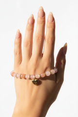 Elegant female hand wearing Love Energy Bracelet with pastel crystal beads and gold heart charm in warm sunlight