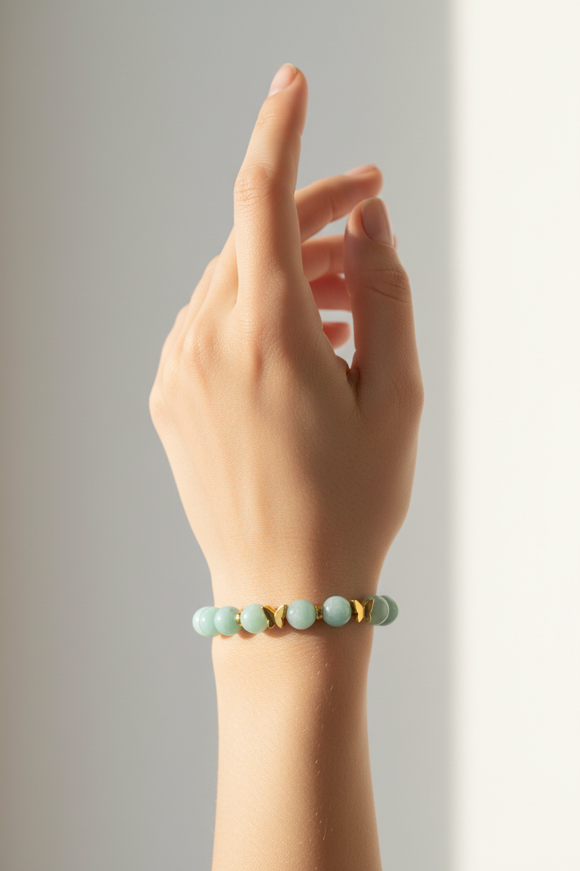 Elegant female hand wearing Serenity Love Bracelet with aquamarine and mint green beads and gold butterfly charm in warm sunlight