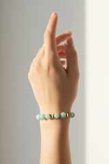 Elegant female hand wearing Serenity Love Bracelet with aquamarine and mint green beads and gold butterfly charm in warm sunlight